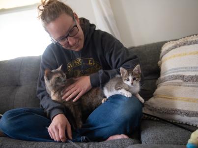 Smiling person sitting on a couch with two kittens