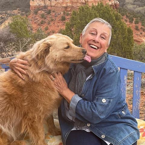 Anne Mejia cuddling with large brown fluffy dog seated on bench in canyon