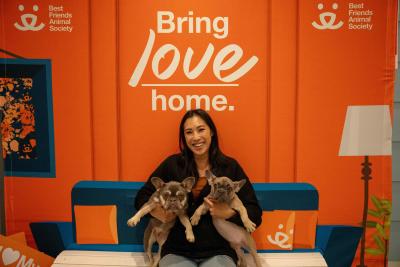 Foster volunteer Jennifer Ung holding both Baby and Celine in front of a wall painted with Bring Love Home