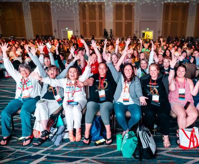 Enthusiastic Best Friends National Conference attendees, sitting for a session, many with their hands up in the air