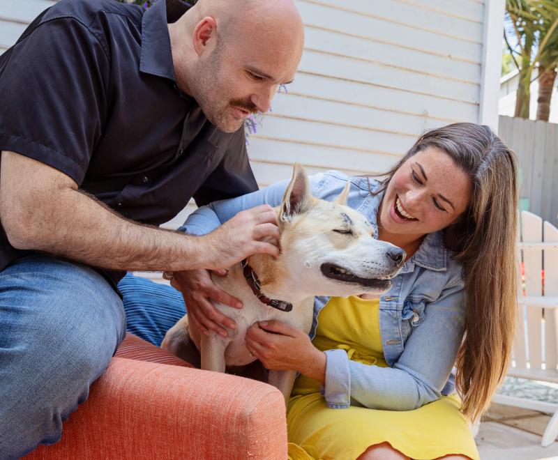Smiling people relaxing on a patio chair with a dog between them