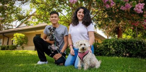 Couple sitting in grass in front of house with two dogs