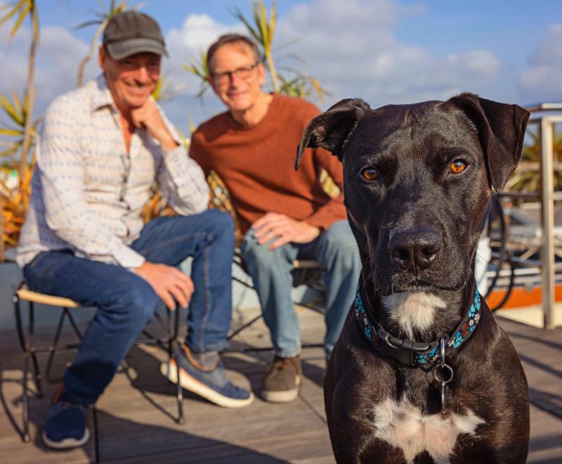 Smiling people sitting outside in a sunny spot with a big dog