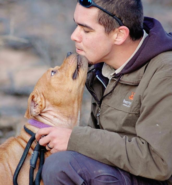 Man getting kiss from brown pit bull terrier in canyon setting