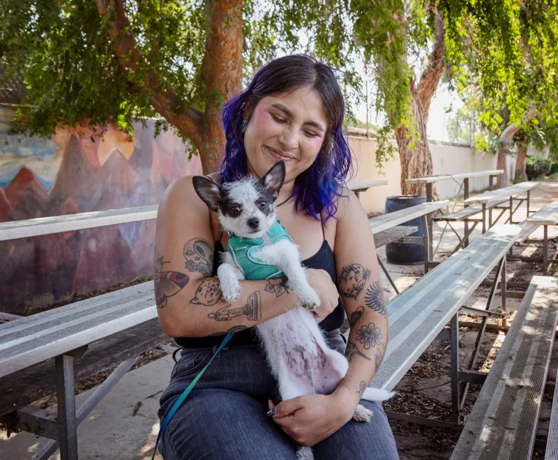 Smiling person holding a small dog in their arms while sitting outside