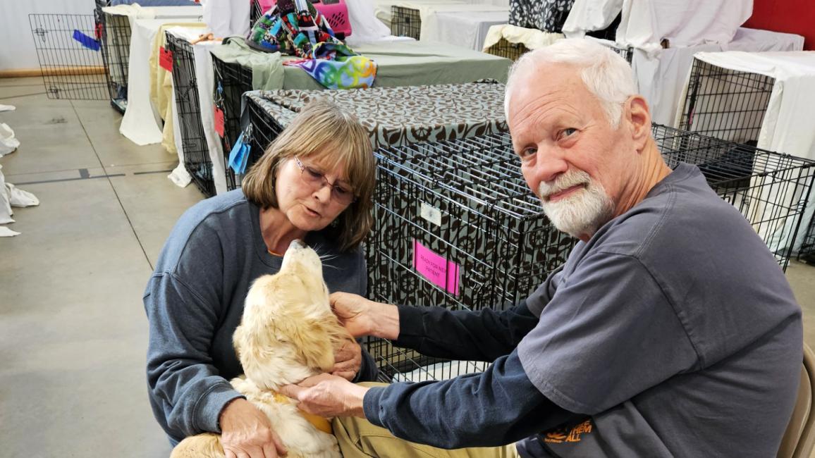 Volunteers Rich and Linda Yates with a dog beside some crates