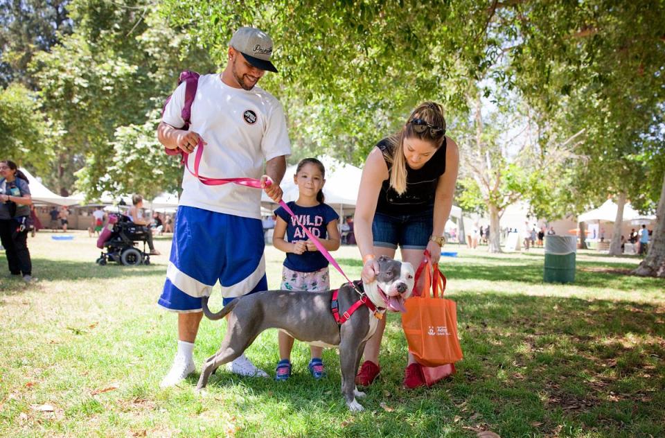 Family of three holding leash to a dog outside.