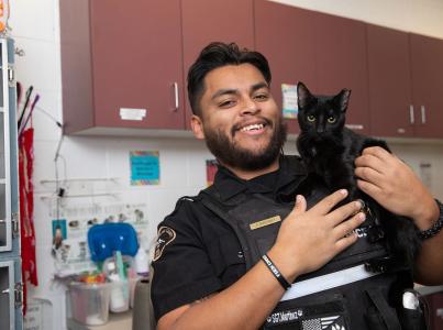 Animal services officer smiles, holding a cat.