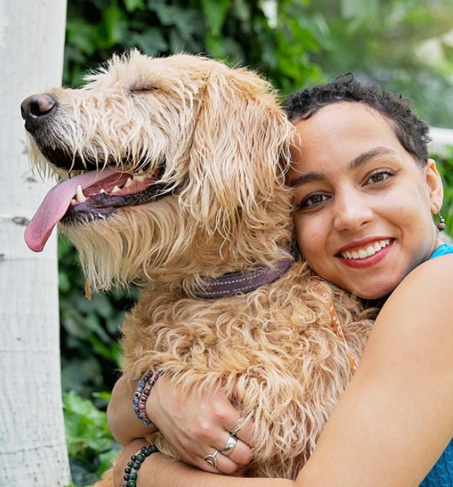 Person hugging a large, tan dog, outside on a lawn