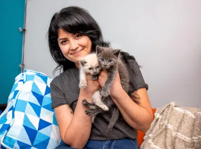 Smiling person holding two tiny kittens next to their face