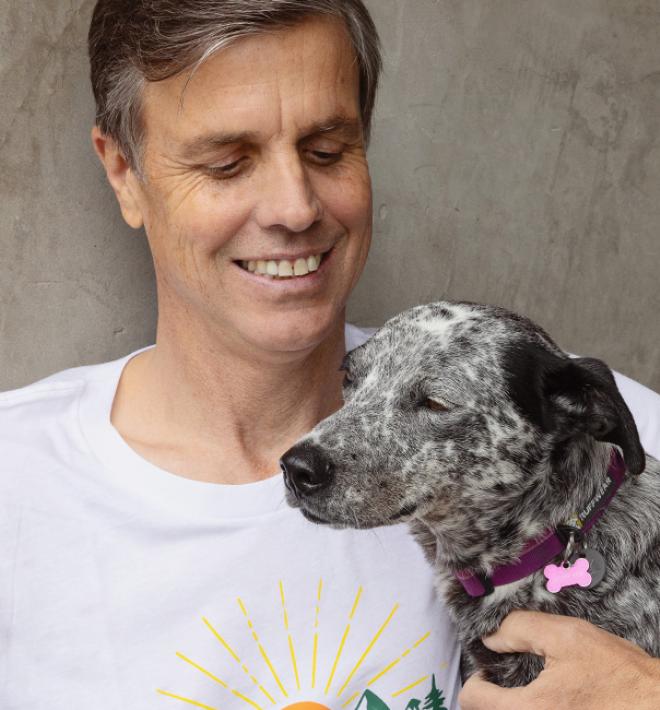 Smiling person sitting outside against a cement wall with a dog