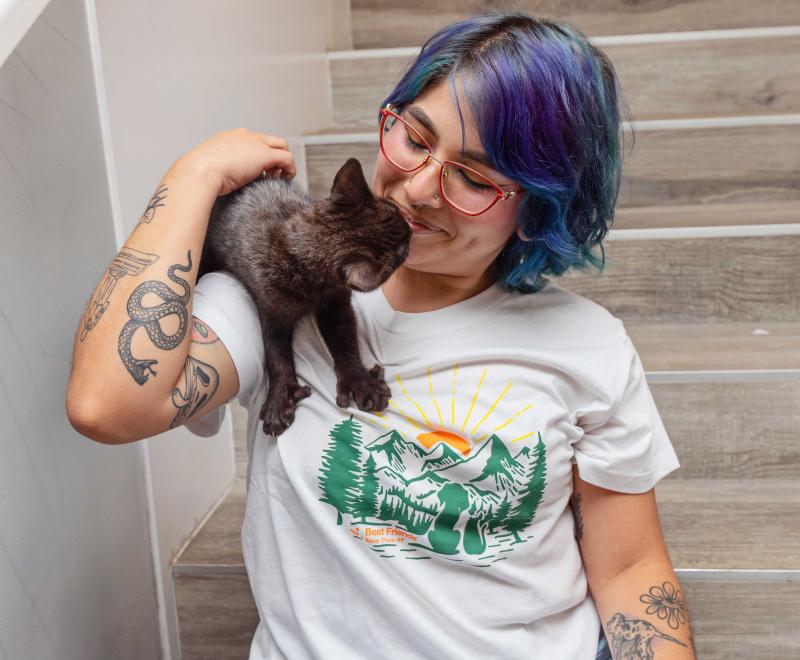 A black kitten on the shoulder of a smiling person wearing a Best Friends T-shirt