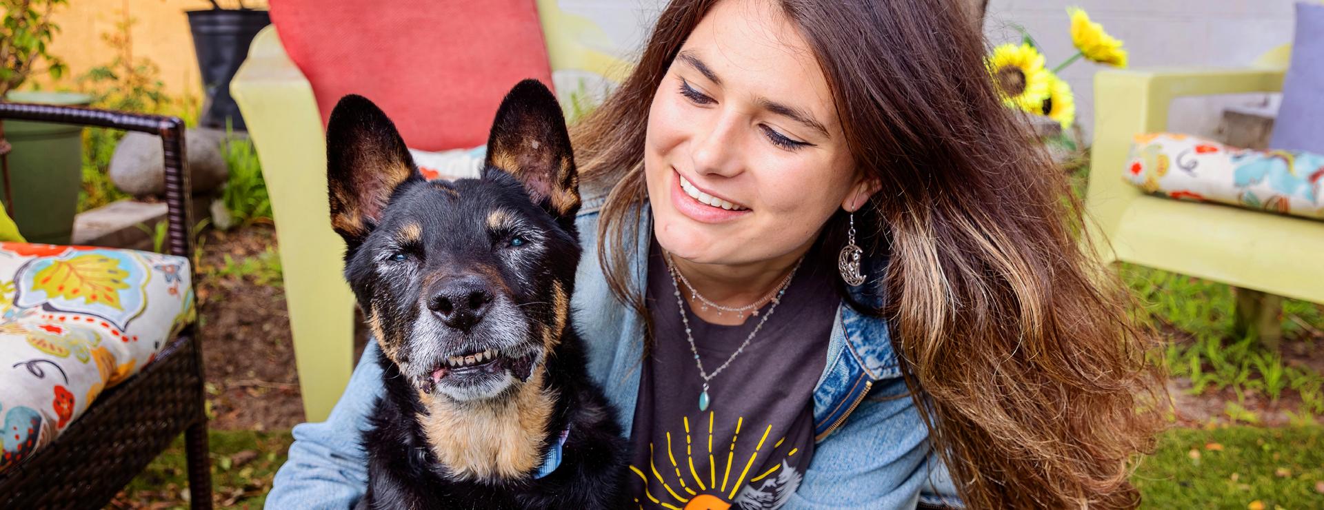 Smiling person sitting on the grass with a senior dog